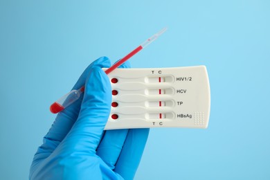 Photo of Doctor holding disposable express test for hepatitis and pipette with blood on light blue background, closeup