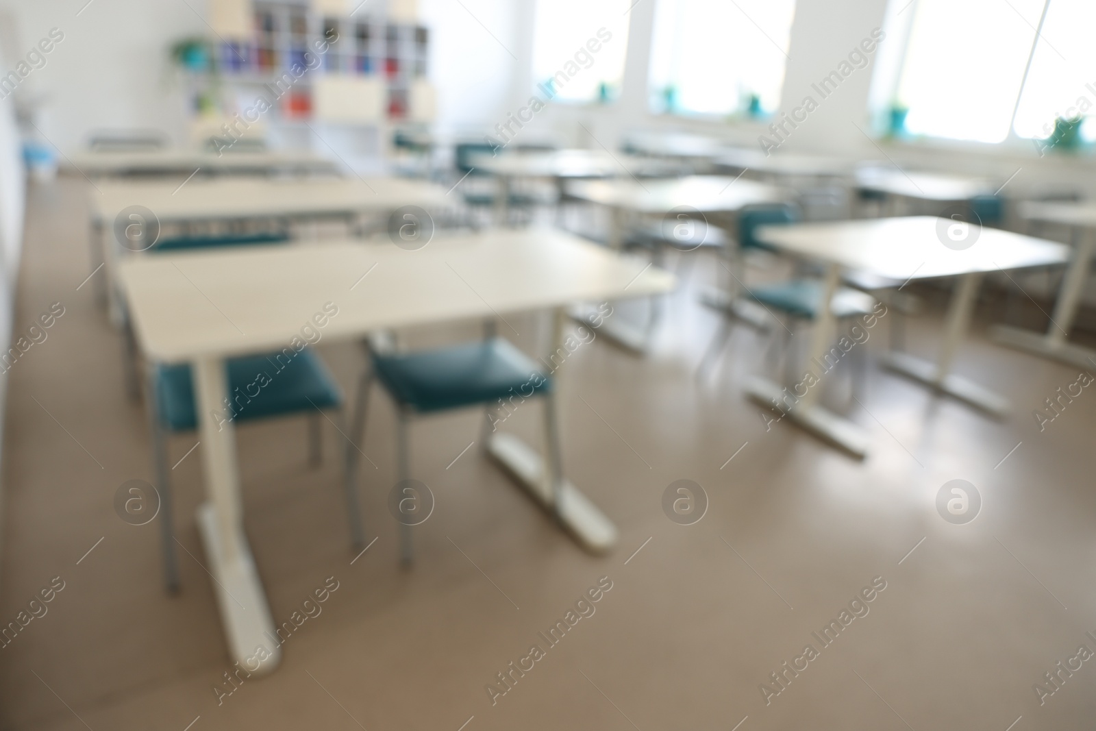 Photo of Blurred view of empty school classroom with desks, windows and chairs