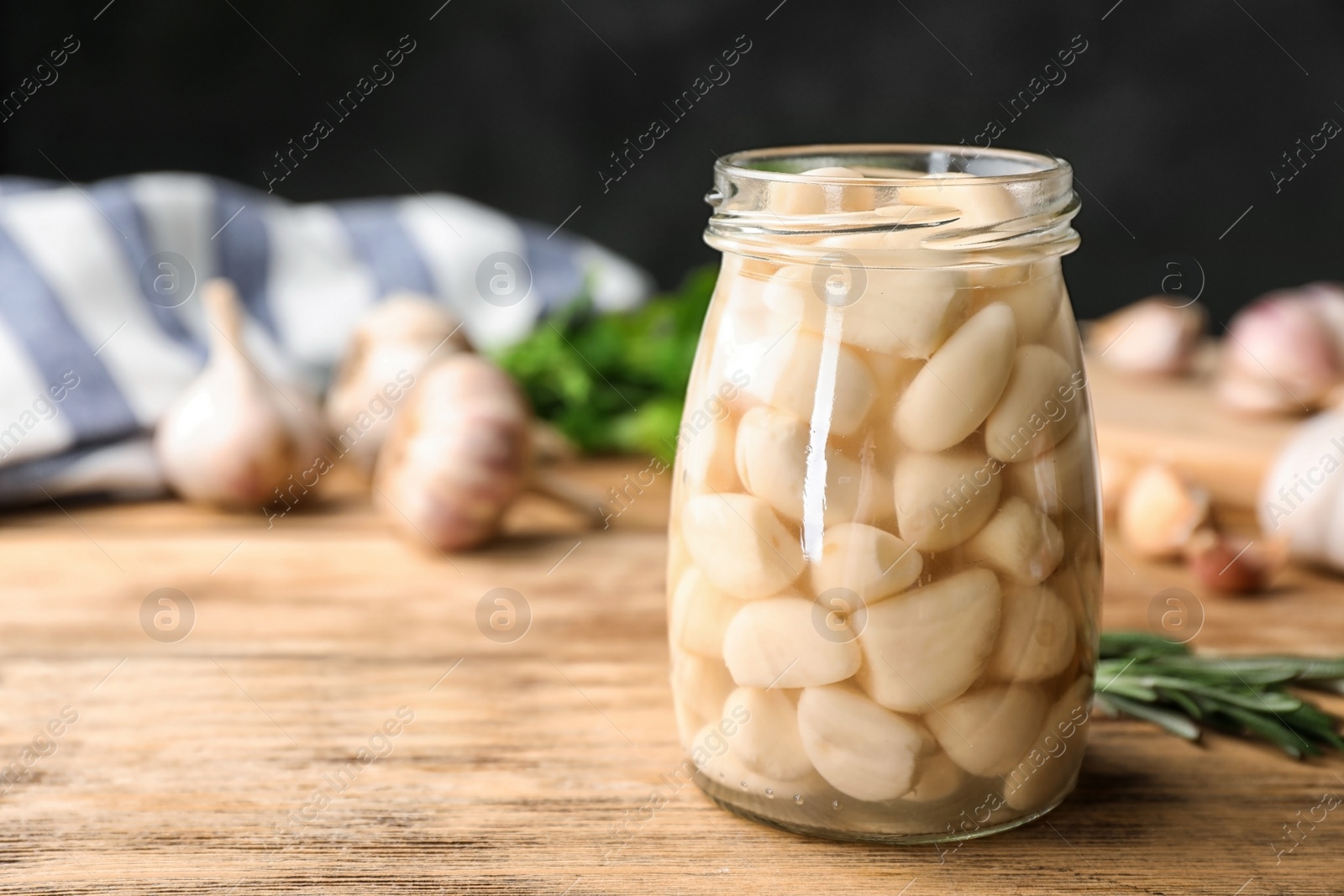 Photo of Preserved garlic in glass jar on wooden table. Space for text