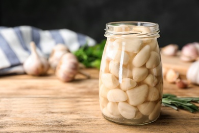 Photo of Preserved garlic in glass jar on wooden table. Space for text