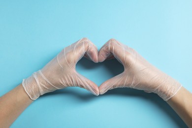 Doctor wearing medical gloves making heart gesture on light blue background, top view