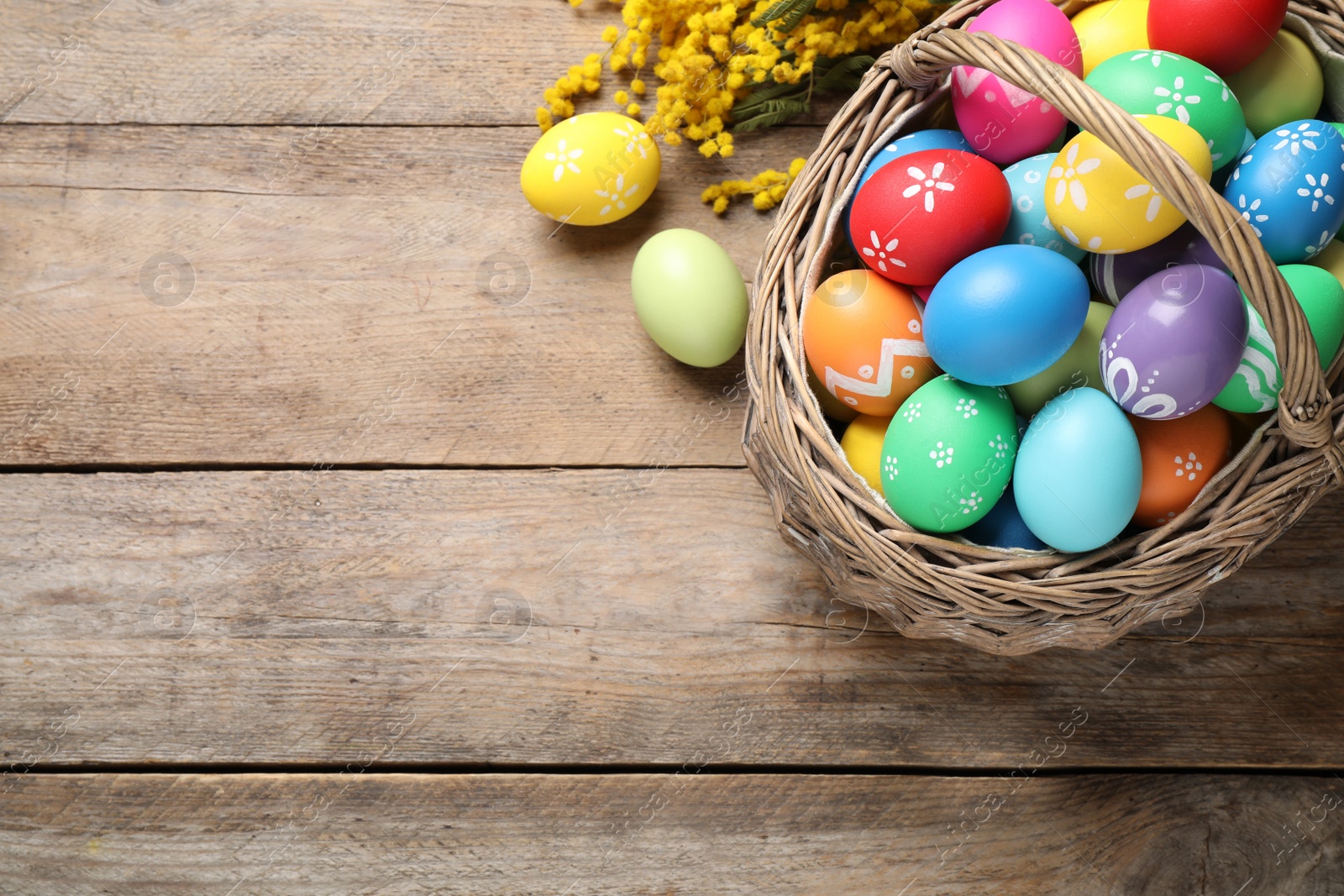 Photo of Colorful Easter eggs and mimosa flowers on wooden background, flat lay. Space for text