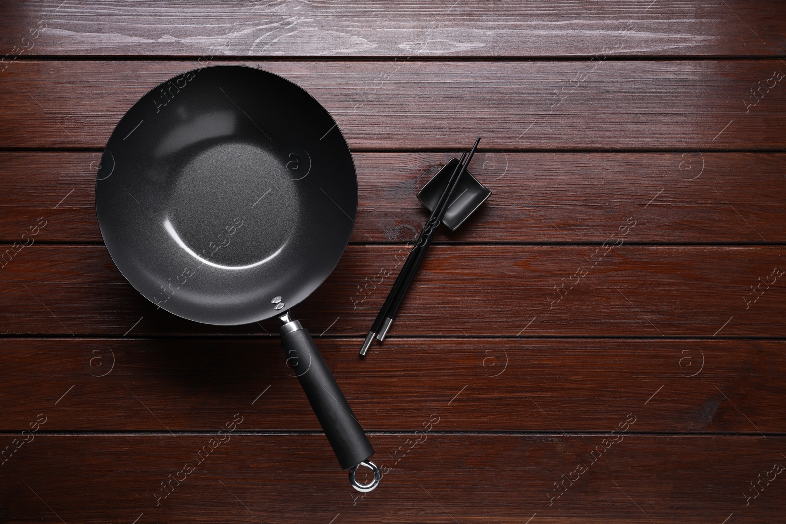 Photo of Empty iron wok and chopsticks on wooden table, flat lay. Space for text