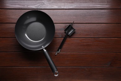 Empty iron wok and chopsticks on wooden table, flat lay. Space for text