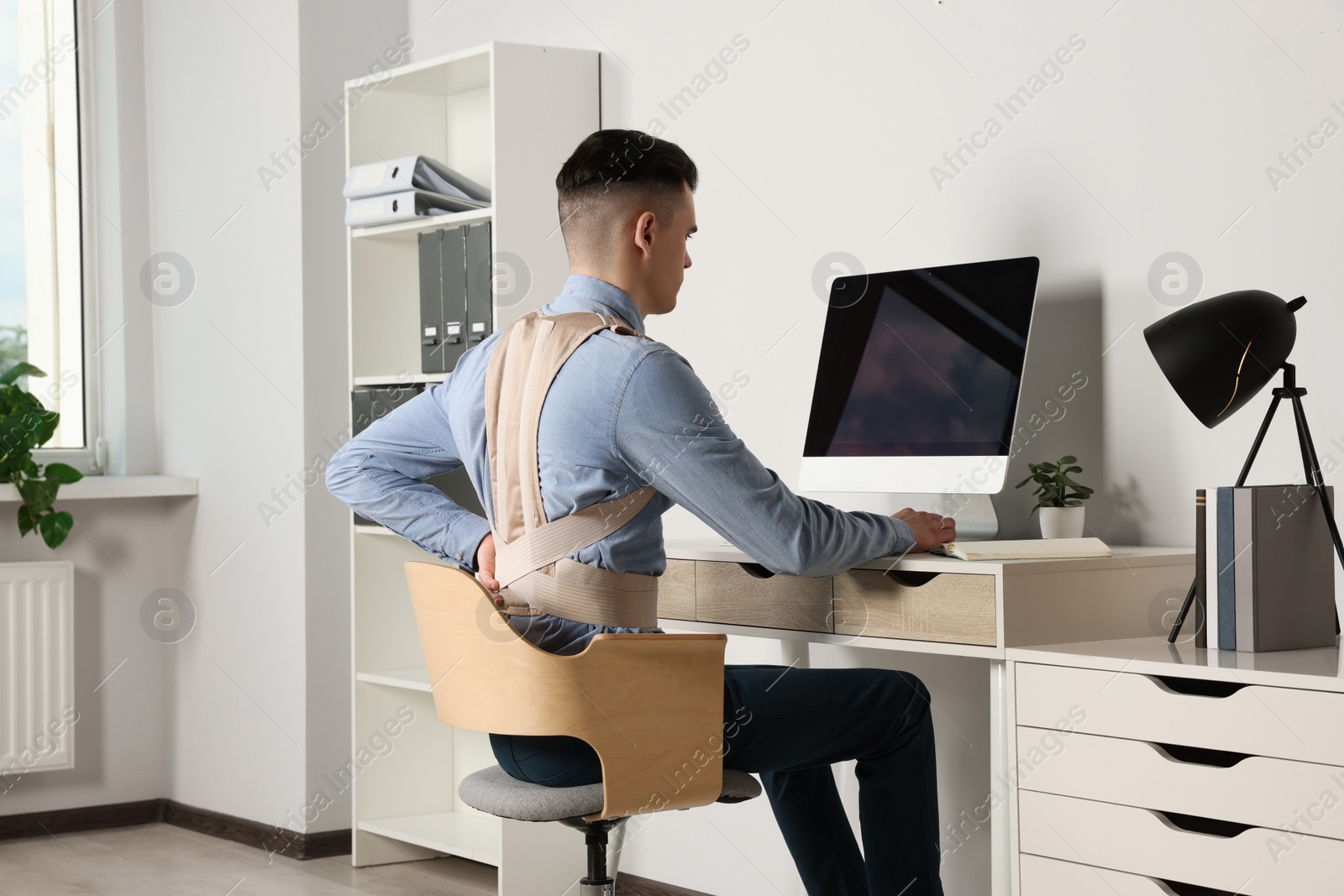 Photo of Man with orthopedic corset working on computer in room