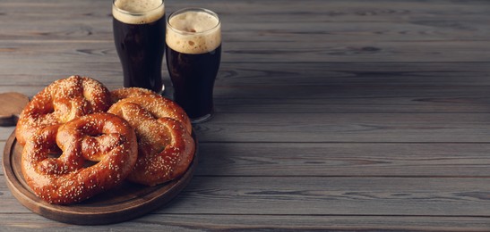 Tasty pretzels and glasses of beer on wooden table, space for text. Banner design