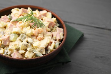 Photo of Tasty Olivier salad with boiled sausage in bowl on grey table, closeup. Space for text
