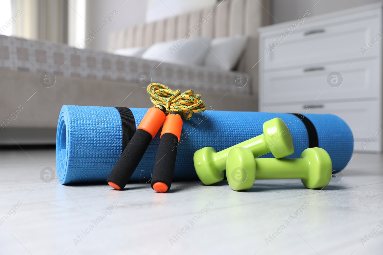 Photo of Dumbbells, skipping rope and yoga mat on floor indoors. Fitness at home