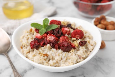 Photo of Oatmeal with freeze dried strawberries and mint on white marble table, closeup