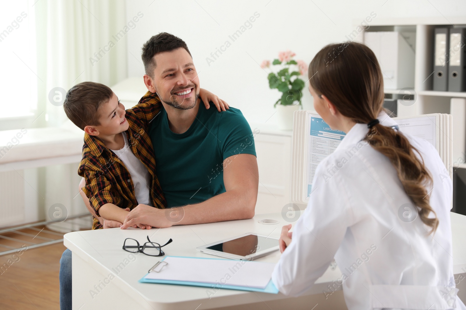 Photo of Father and son visiting pediatrician. Doctor working with little patient in hospital