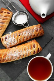 Fresh tasty puff pastry with sugar powder and tea served on grey table, flat lay