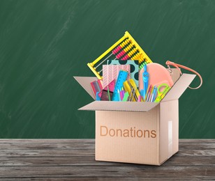 Image of Donation box with different school stationery on wooden table near chalkboard