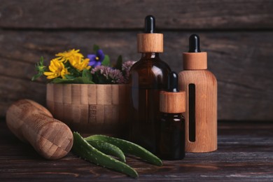 Photo of Glass bottles of aromatic essential oil and mortar with different herbs on wooden table, closeup