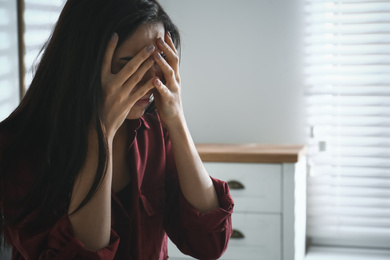 Photo of Abused young woman crying indoors, space for text. Domestic violence concept