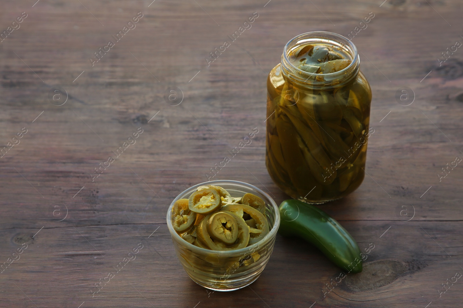 Photo of Fresh and pickled green jalapeno peppers on wooden table. Space for text