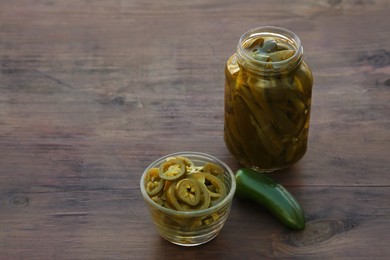 Photo of Fresh and pickled green jalapeno peppers on wooden table. Space for text