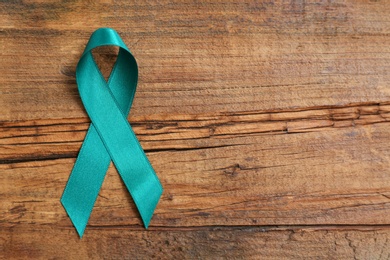 Photo of Teal awareness ribbon on wooden background, top view with space for text. Symbol of social and medical issues