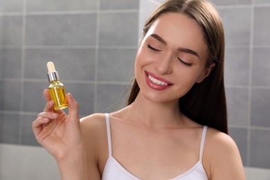 Young woman with bottle of essential oil in bathroom