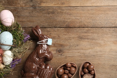 Photo of Chocolate  bunny with protective mask, eggs, wreath and space for text on wooden table, flat lay. Easter holiday during COVID-19 quarantine
