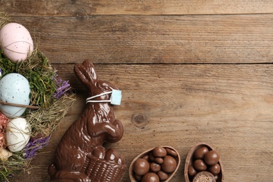 Chocolate  bunny with protective mask, eggs, wreath and space for text on wooden table, flat lay. Easter holiday during COVID-19 quarantine