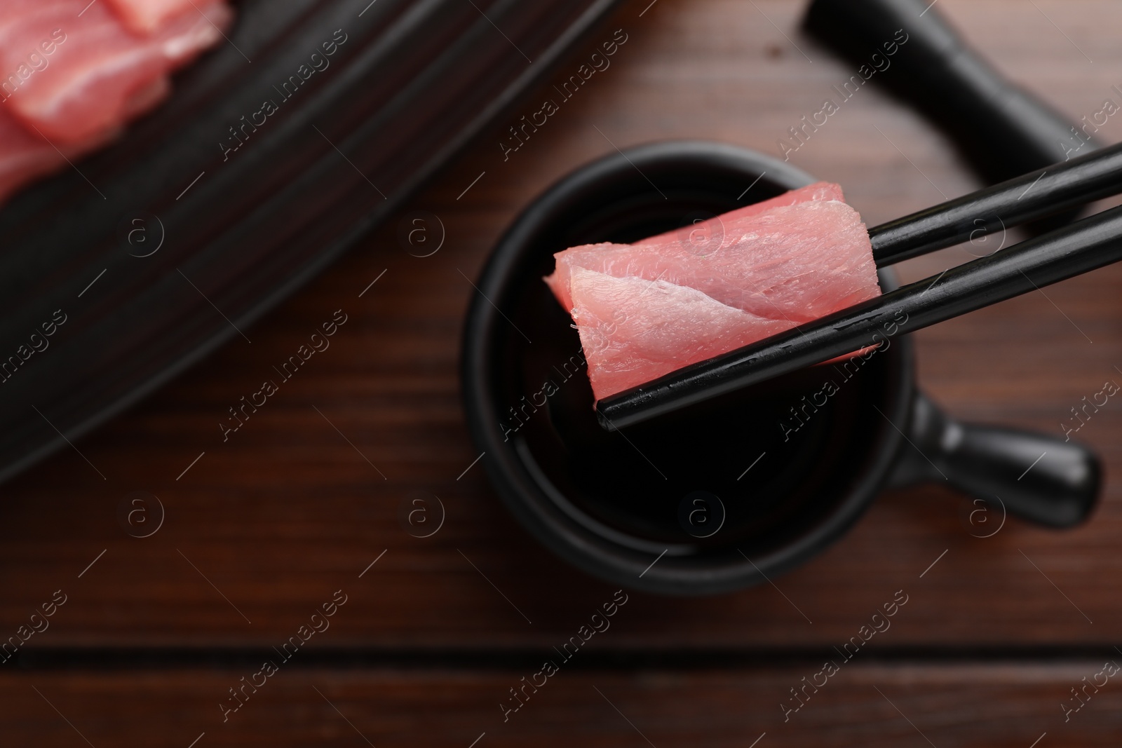 Photo of Holding tasty sashimi (piece of fresh raw tuna) with chopsticks over table, top view