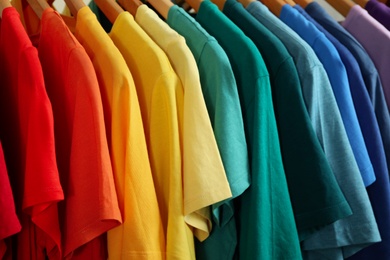 Hangers with bright clothes as background, closeup. Rainbow colors