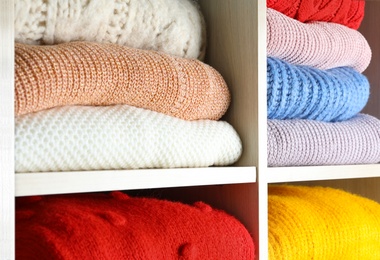 Folded colorful winter sweaters on shelves as background