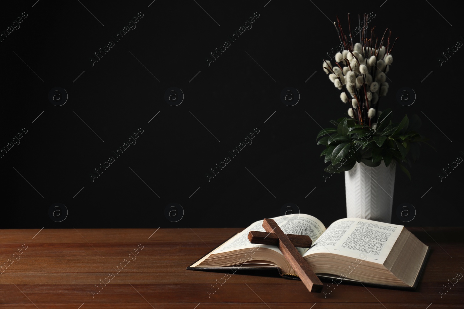 Photo of Bible, plant with willow branches and cross on wooden table, space for text