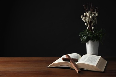 Bible, plant with willow branches and cross on wooden table, space for text