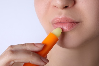 Photo of Woman applying hygienic lipstick on lips against white background, closeup