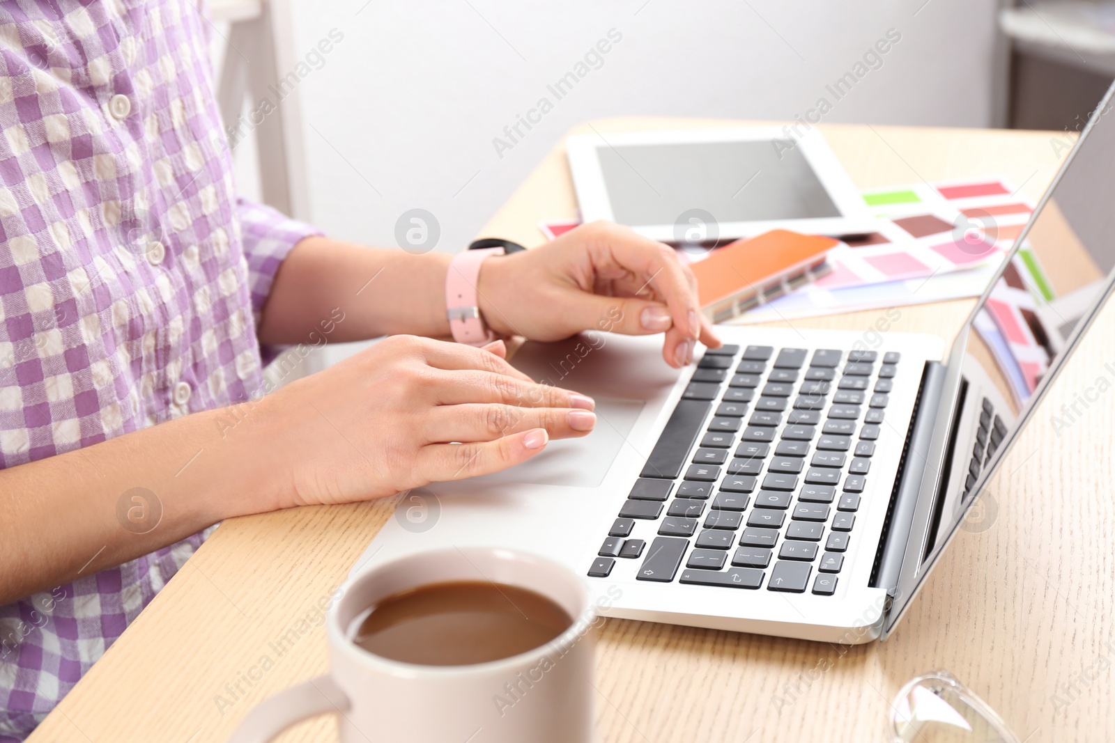 Photo of Woman working with laptop and palette samples at wooden table, closeup