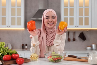 Photo of Muslim woman making delicious salad with vegetables at white table in kitchen
