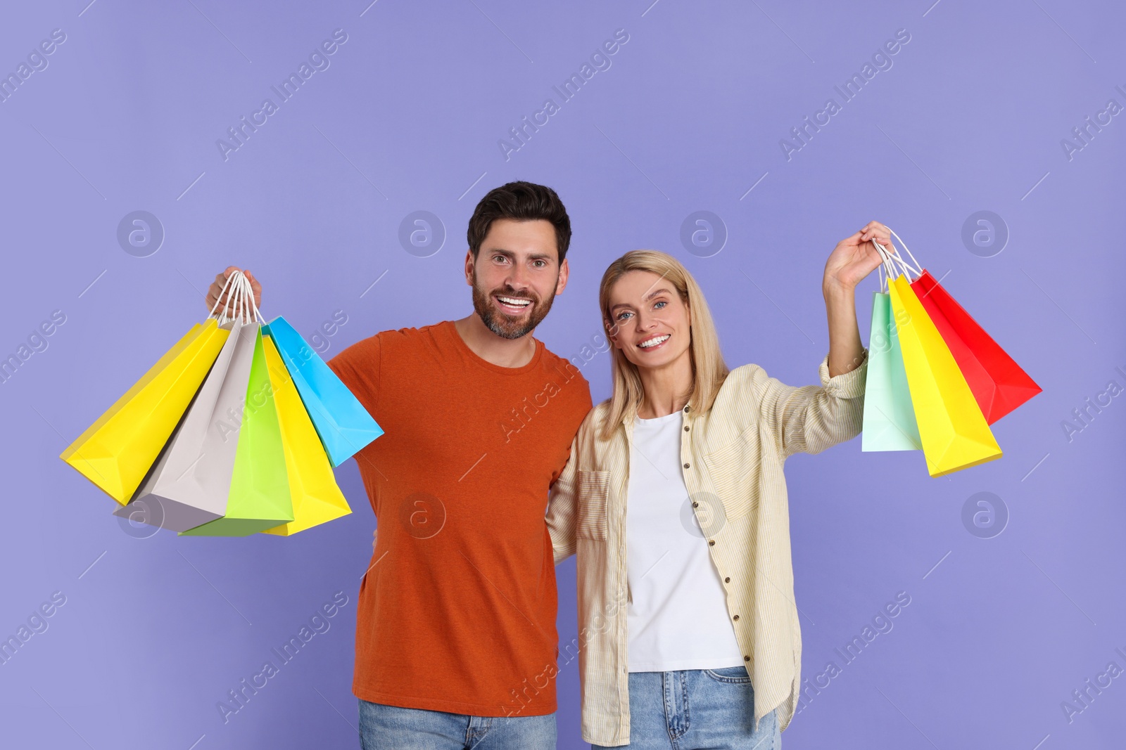 Photo of Family shopping. Happy couple with many colorful bags on violet background