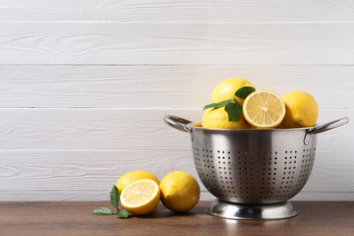 Fresh lemons and green leaves on wooden table. Space for text