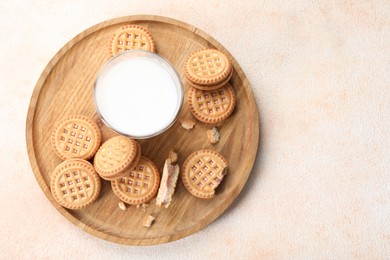 Photo of Tasty sandwich cookies with cream and glass of milk on beige background, top view. Space for text