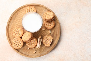 Tasty sandwich cookies with cream and glass of milk on beige background, top view. Space for text