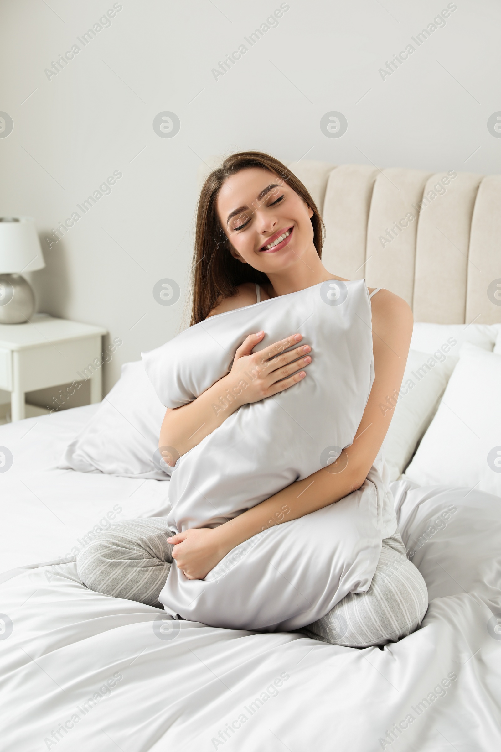 Photo of Young woman hugging pillow on comfortable bed with silky linens