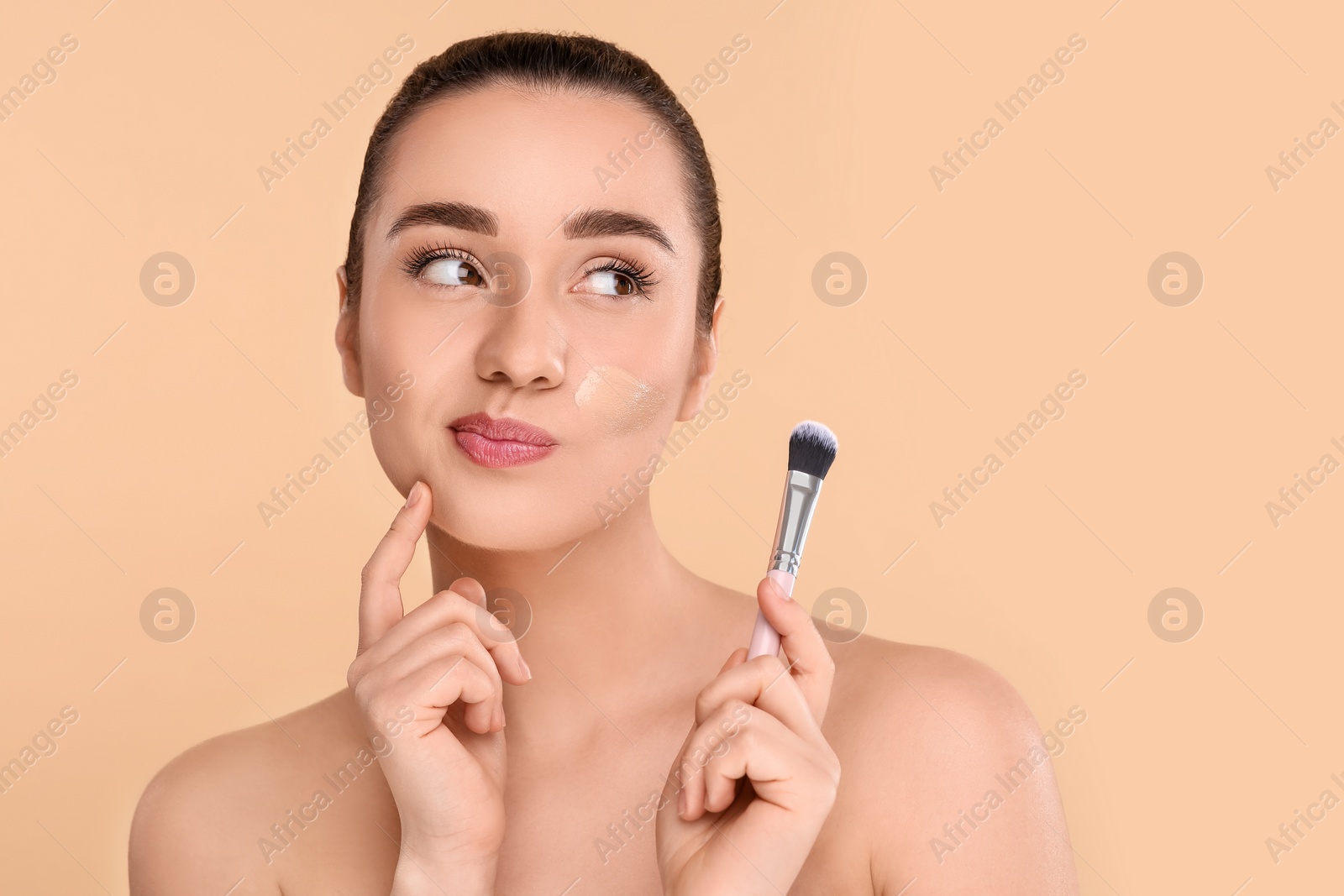 Photo of Woman with swatch of foundation holding makeup brush on beige background