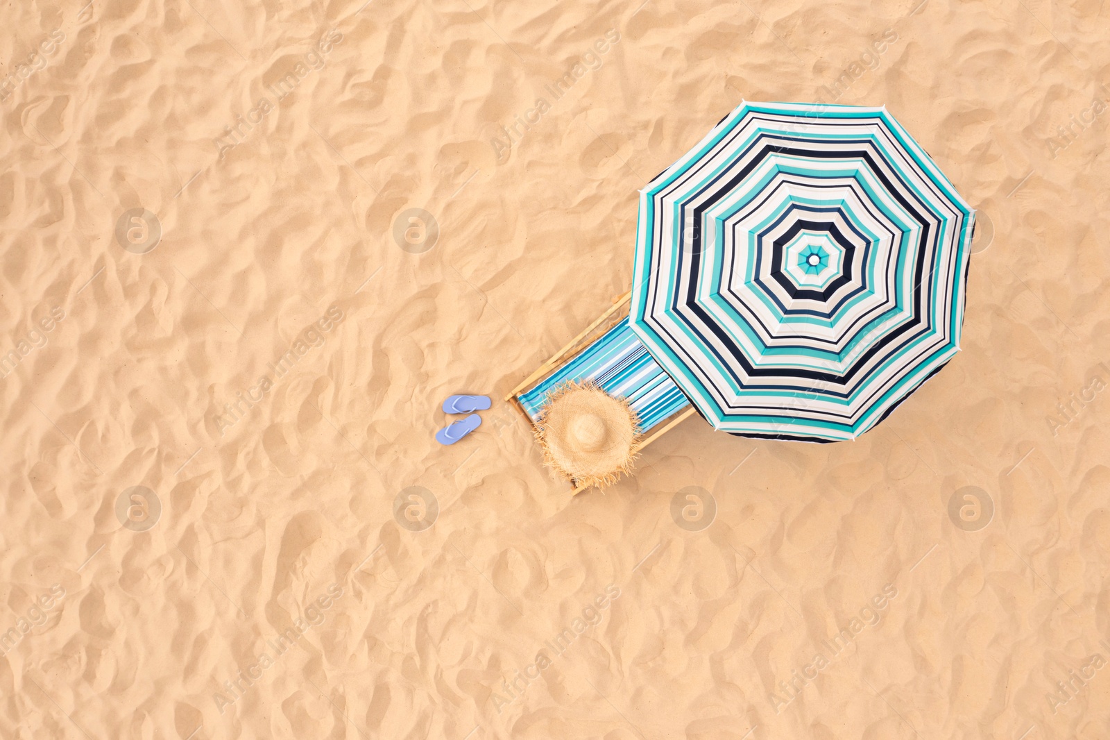 Image of Striped beach umbrella near sunbed with vacationist's stuff on sandy coast, aerial view. Space for text