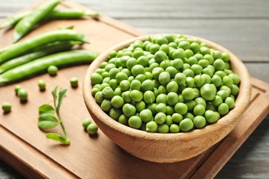 Photo of Bowl with green peas on wooden board