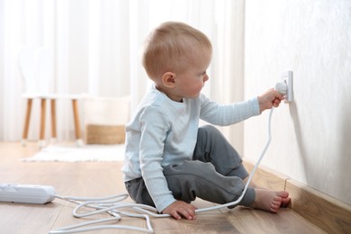 Little child playing with electrical socket and power strip plug at home. Dangerous situation