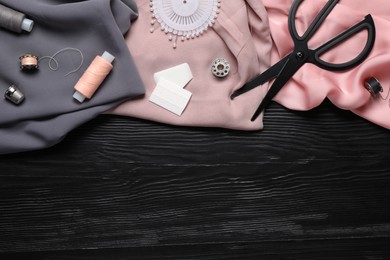 Flat lay composition with sewing accessories on black wooden background, space for text