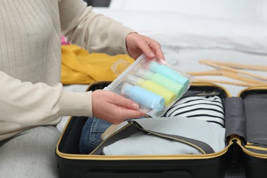 Photo of Woman with plastic bag of cosmetic travel kit packing suitcase, closeup. Bath accessories