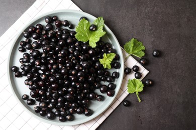 Plate with ripe blackcurrants and leaves on grey background, flat lay. Space for text