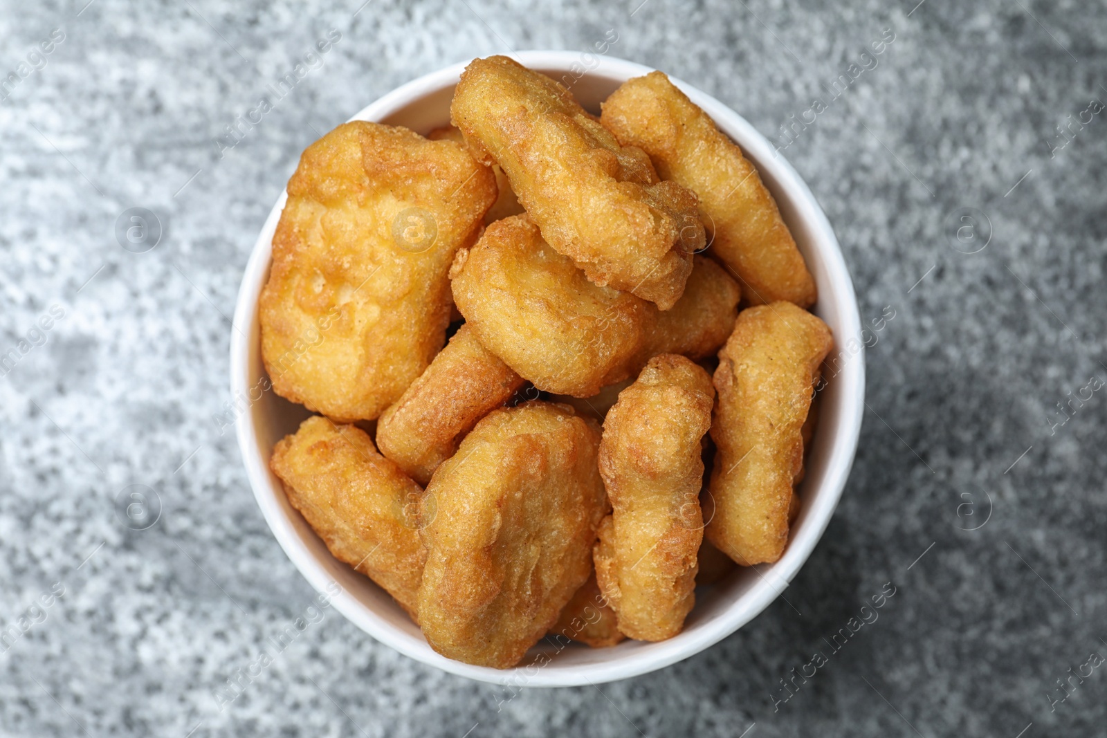 Photo of Bucket with tasty chicken nuggets on grey table, top view