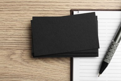 Photo of Blank black business cards, notebook and pen on wooden table, top view. Mockup for design