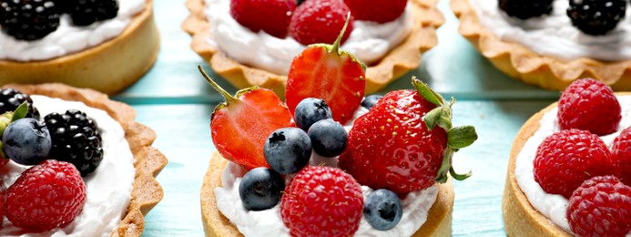 Image of Delicious tartlets with fresh berries on light blue wooden table, closeup. Banner design