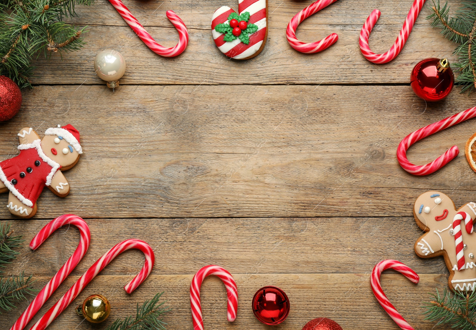 Photo of Frame of tasty candy canes and Christmas decor on wooden table, flat lay. Space for text