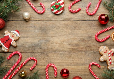 Photo of Frame of tasty candy canes and Christmas decor on wooden table, flat lay. Space for text