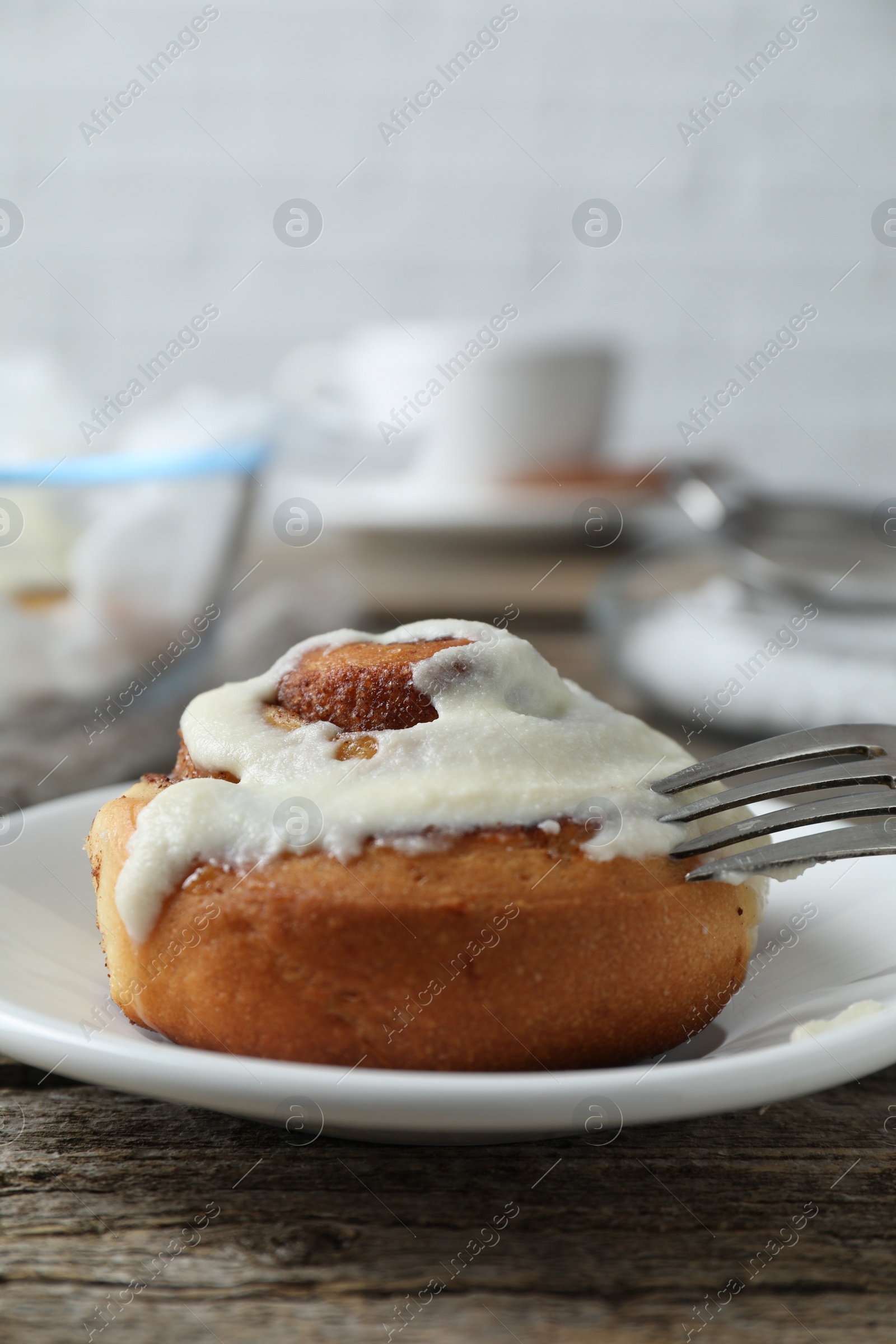 Photo of Tasty cinnamon roll with cream on wooden table, closeup. Space for text